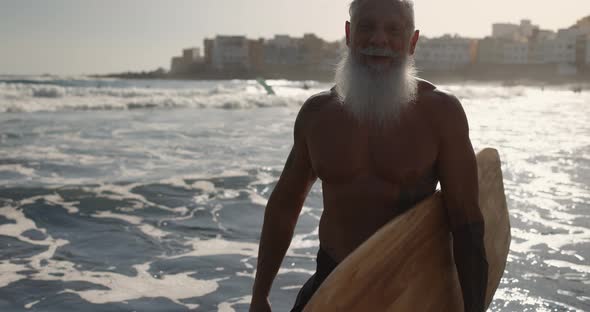 Senior fit surfer man holding surfboard on the beach - Concept of extreme sport