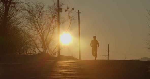 The Guy Runs Down the Hill on the Road at Dawn. The Glare of the Sun. Cold Weather.  Ultra 