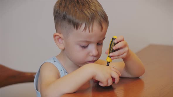 Shooting a Portrait of a Cute Preschool Boy, the Child Repairs His Favorite Red Toy Car for Kids