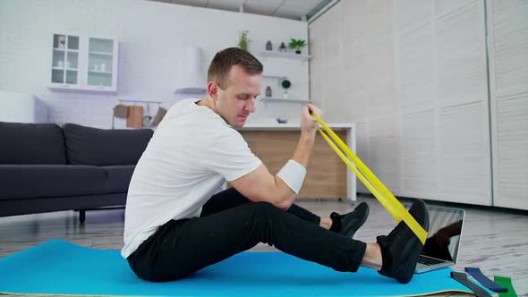 Man doing exercises at home. Man sitting on the floor at home and doing exercises with spander
