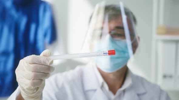 PCR Test in Laboratory Aged Doctor Looking at COVID19 Swab Collection Kit Greyhaired Lab Worker