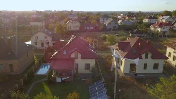 Aerial view of a residential private house with solar panels on roof and wind generator turbine