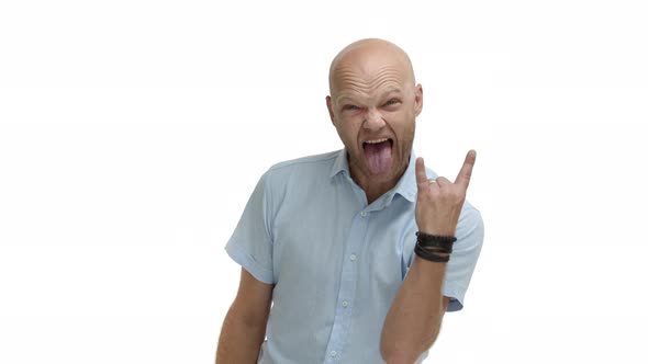 Handsome Bald Guy with Bristle Having Fun Showing Rocknroll Gesture and Sticking Tongue Standing