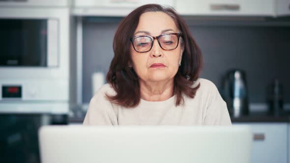 Serious Senior Woman in Glasses Working at Home with a Laptop