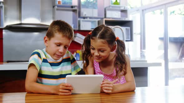 Siblings giving high five to each other while using digital tablet in kitchen alt