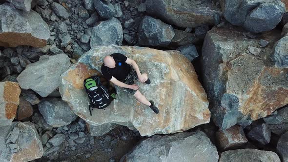 Bald Man lays on a large stone. Tourist with a backpack in shorts and t-shirt is resting.