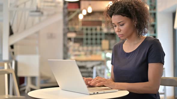 Young African Woman Reacting to Loss on Laptop in Cafe