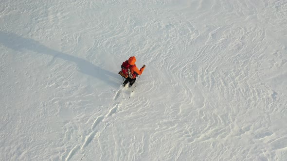 Aerial Footage a Man with a Backpack and Sticks Walks Through the Snowy Desert Leaving a Chain of