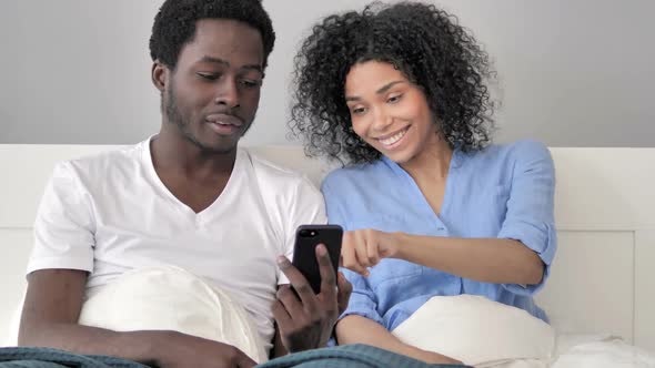 African Couple Using Smartphone Together in Bed