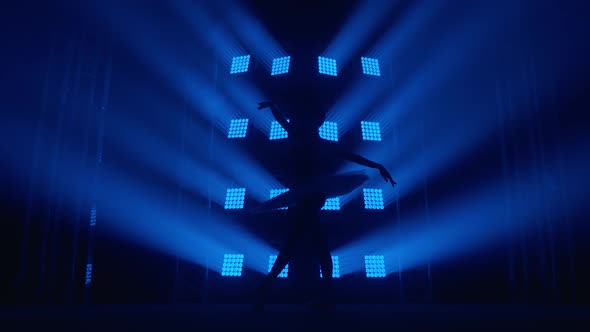 Graceful Silhouette Ballerina Doing a Workout in the Classroom. Smoke in the Rays of Blue Light