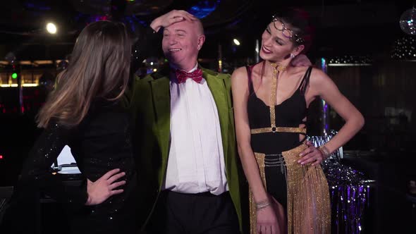 Middle Shot of Two Young Beautiful Caucasian Women Posing with Elderly DJ in Night Club, Happy