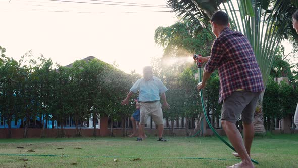 Happy Family playing together during Retired Grandfather watering the plants at the home garden.