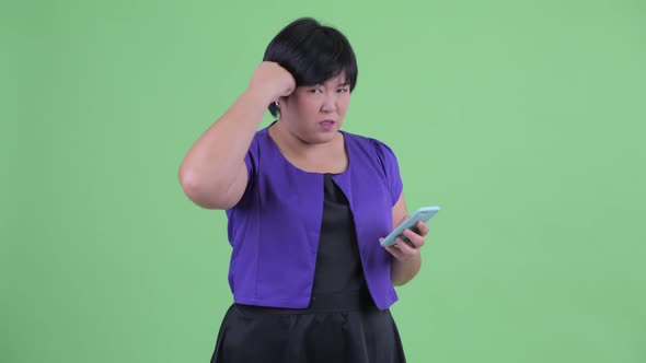 Stressed Young Overweight Asian Woman Using Phone and Getting Bad News