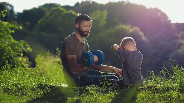 Father and Little Son Lifting Dumbbells Outdoors