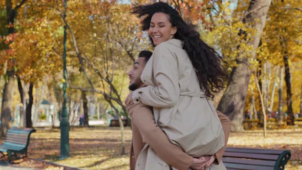 Hispanic Guy Spins Holding Piggyback Girl Brunette Woman Hug Male By Shoulders Young Couple Laughing