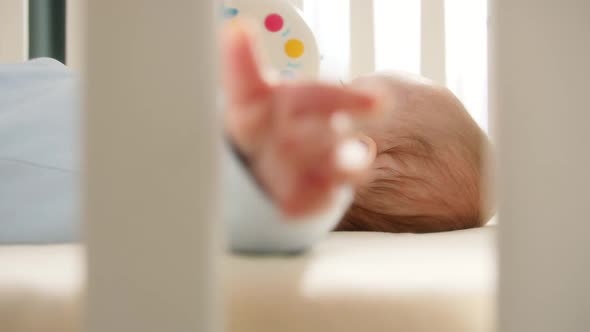 Baby Lying in Crib and Holding Wooden Banister with Hand