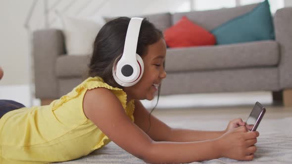 Happy hispanic girl watching video on tablet wearing head phones lying on floor