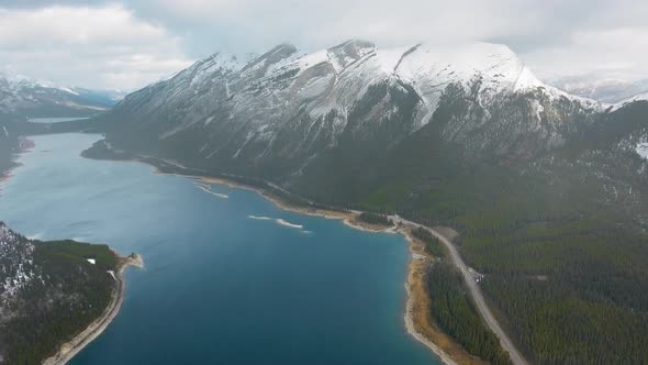 Drone shoots the cloudy sky and snowy peaks reflected in Spray Lakes Reservoir, Alberta, Canada