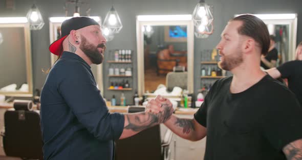 Two Young Bearded and Mustashed Men with Tattoed Hands are Shaking Hands and Hugging Each Other in