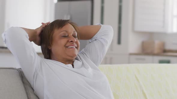 Happy african american senior woman leaning back on couch with eyes closed, smiling