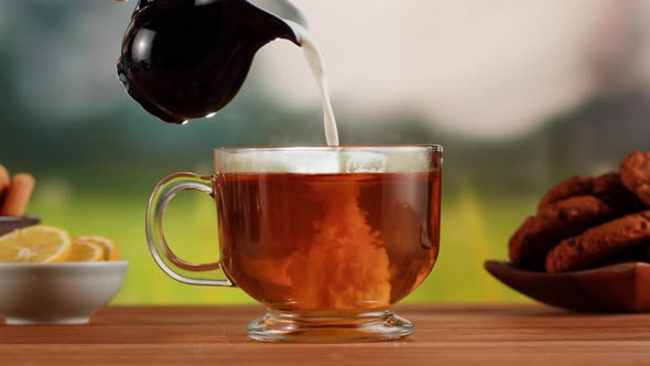 Pouring Milk Into Black Tea in Glass Cup on a Wooden Table