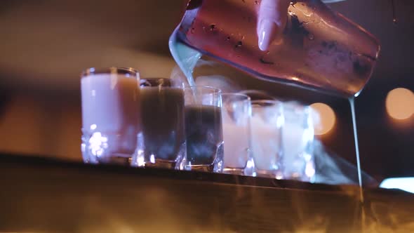 dry ice smoking shot glasses filling up with colorful cocktail (super slow motion)