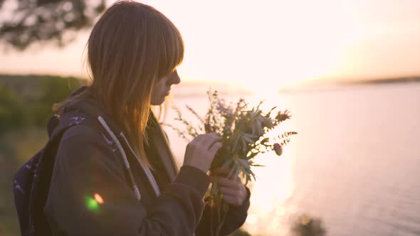 Beautiful Young Woman with a Bouquet of Wildflowers on the Coast at Sunset