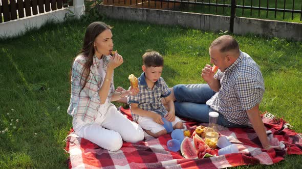 Happy Young Woman and Man Sit with Little Boy on Lawn