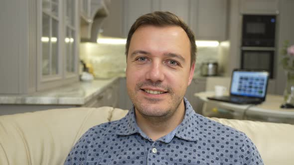 Young Adult Male Sitting on Sofa at Home Looks at Camera and Greets Colleagues Makes Live Video