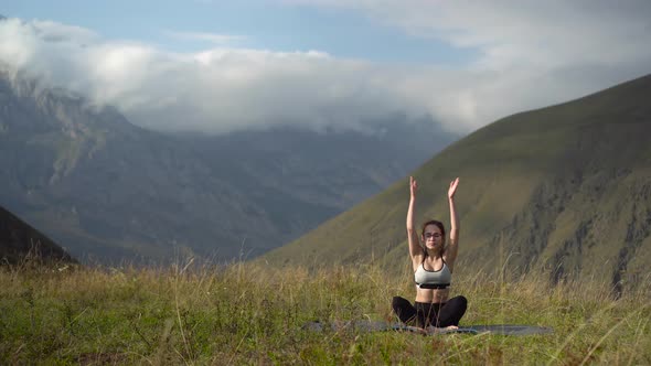 A Young Woman in a Tracksuit Practices Yoga in the Mountains.