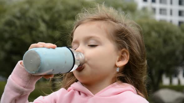 Close Up Little Girl Drinks Water From a Bottle in a Summer City