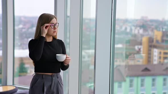 Beautiful female with cup of coffee standing by the window