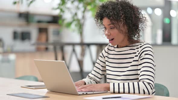 African Woman Celebrating Success on Laptop in Office