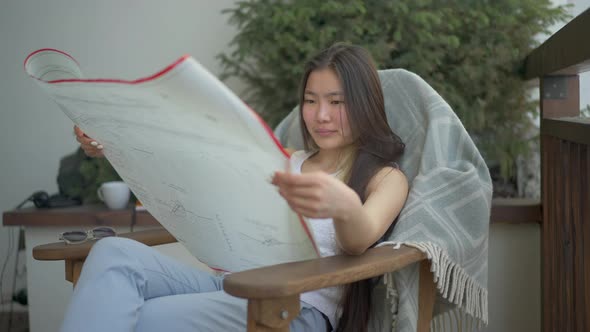Talented Young Asian Woman Examining Architectural Blueprint Sitting on Armchair on Deck