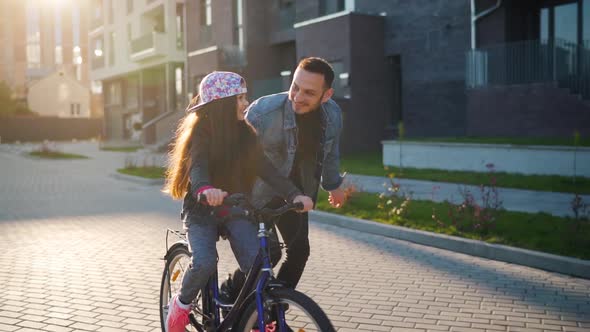 Dad Is Teaching Daughter How To Ride Bicycle at Sunset. Slow Motion