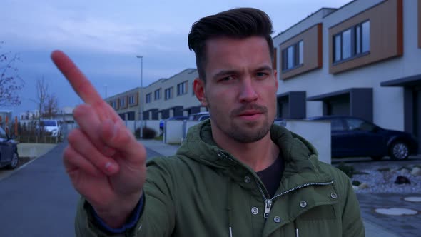 A Young Man Stands on a Road in a Neighborhood and Shakes a Finger in a Sign of Disapproval