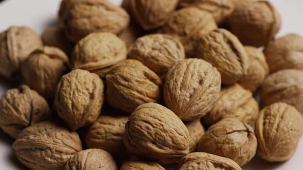 Cinematic, rotating shot of walnuts in their shells on a white surface - WALNUTS 