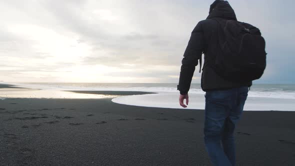 Man Traveler Walking on Volcanic Black Sand Beach in Iceland