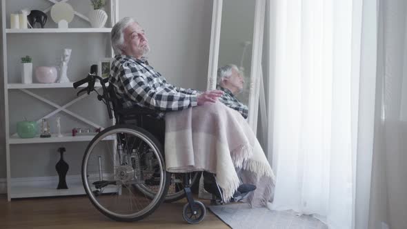 Side View of Mature Caucasian Grey-haired Man Sitting in Wheelchair and Thinking. Lonely Elderly Man