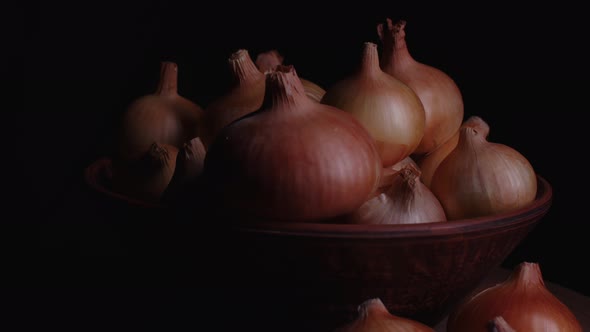 Pile of whole bulbs of raw onion in ceramic bowl on table.