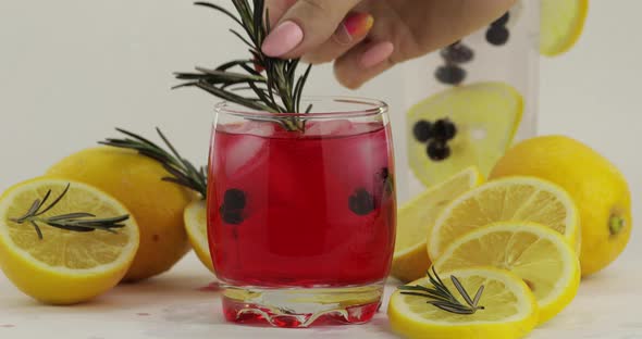 Adding Rosemary Branch in a Glass with Soda Lemonade Red Cocktail