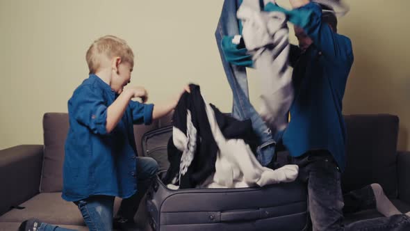 Joyful boys wearing identically are taking out clothes of the packed suitcase.