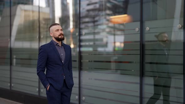 a Mustachioed and Bearded Man in a Plaid Suit Has Hands in Pockets and is Walking Along the Glass