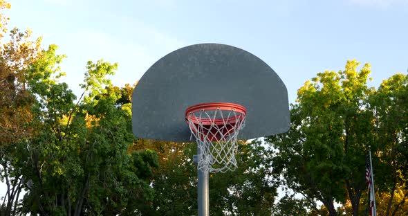 Slide right shot of a basketball hoop with metal backboard and and orange rim in an empty park court