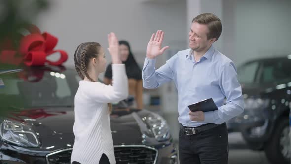 Cheerful Car Dealer and Joyful Little Girl Giving High Five in Slow Motion in Car Dealership