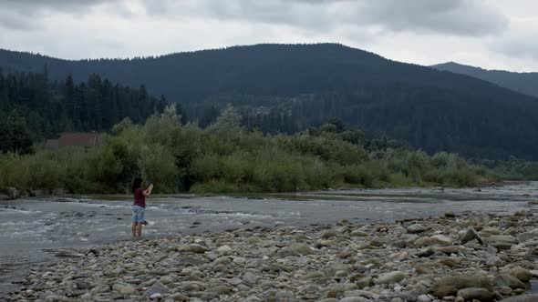 Lovely Girl Photographs a Panorama of a Mountain Landscape by a Mountain River on a Cloudy Evening