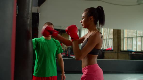 Sporty Fit African Female Fighter with Boxing Coach Working Out on Heavy Bag