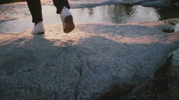 Back View of Female Legs Carefully Stepping Over Small Beautiful Water Stream on a Rock