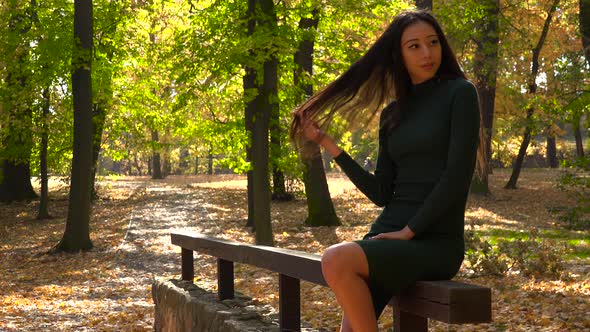 A Young Asian Woman Sits on A Wooden Railing in A Park and Strikes Poses for A Camera