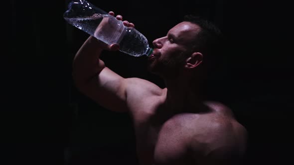 Strong Shirtless Man Drinking Water From the Plastic Bottle in the Dark